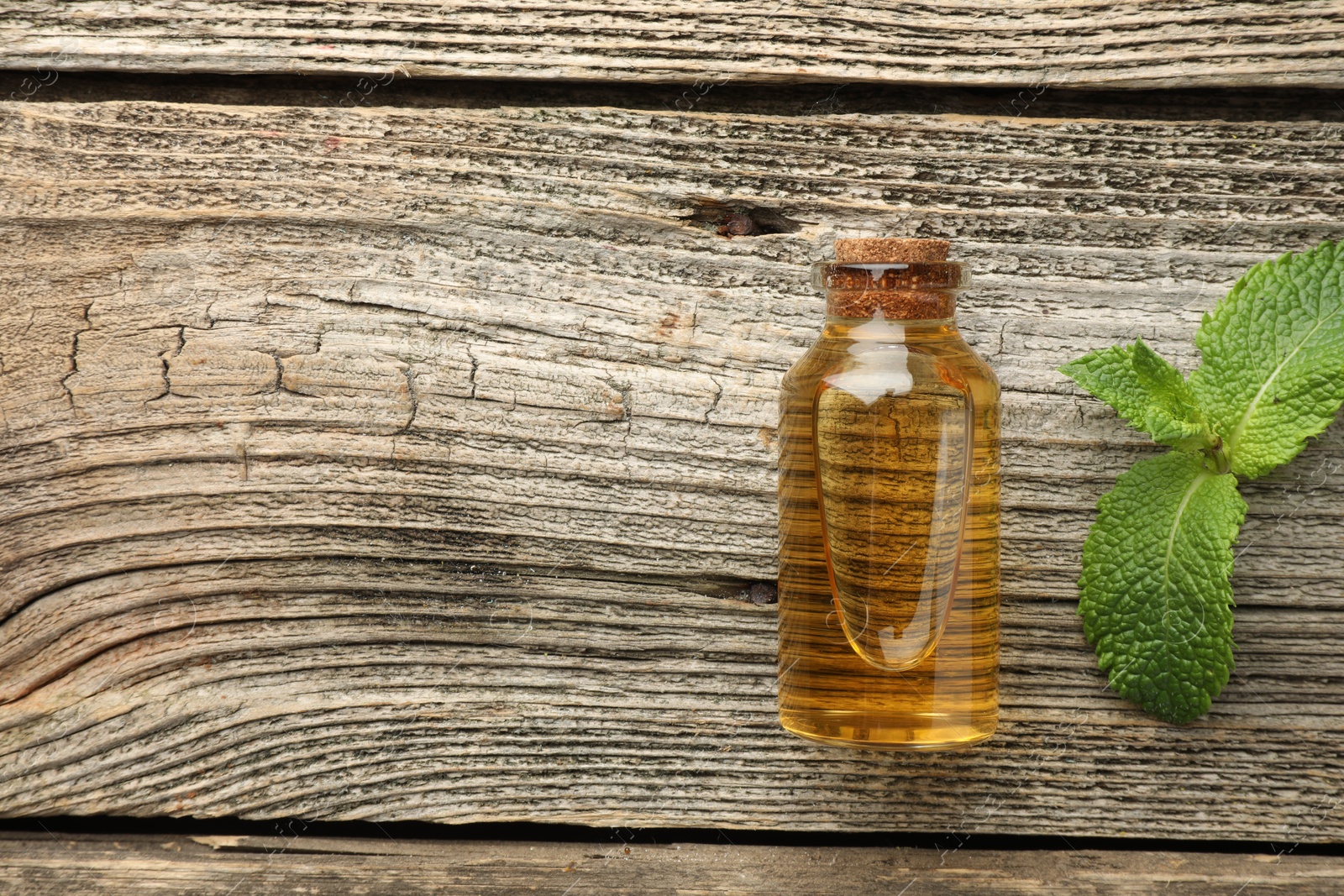 Photo of Bottle of mint essential oil and fresh leaves on wooden table, top view. Space for text