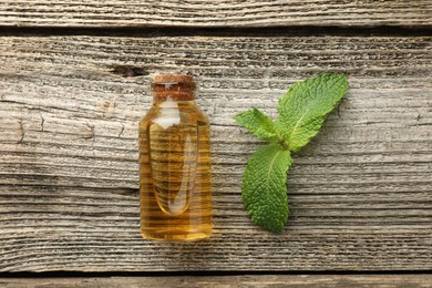 Photo of Bottle of mint essential oil and fresh leaves on wooden table, top view