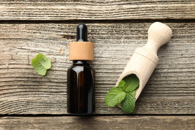 Photo of Bottle of mint essential oil and fresh leaves on wooden table, top view