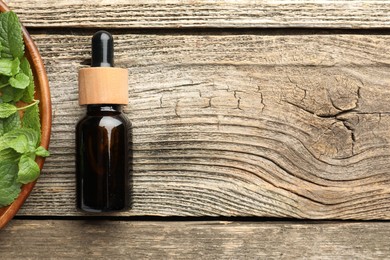 Photo of Bottle of mint essential oil and fresh leaves on wooden table, top view. Space for text