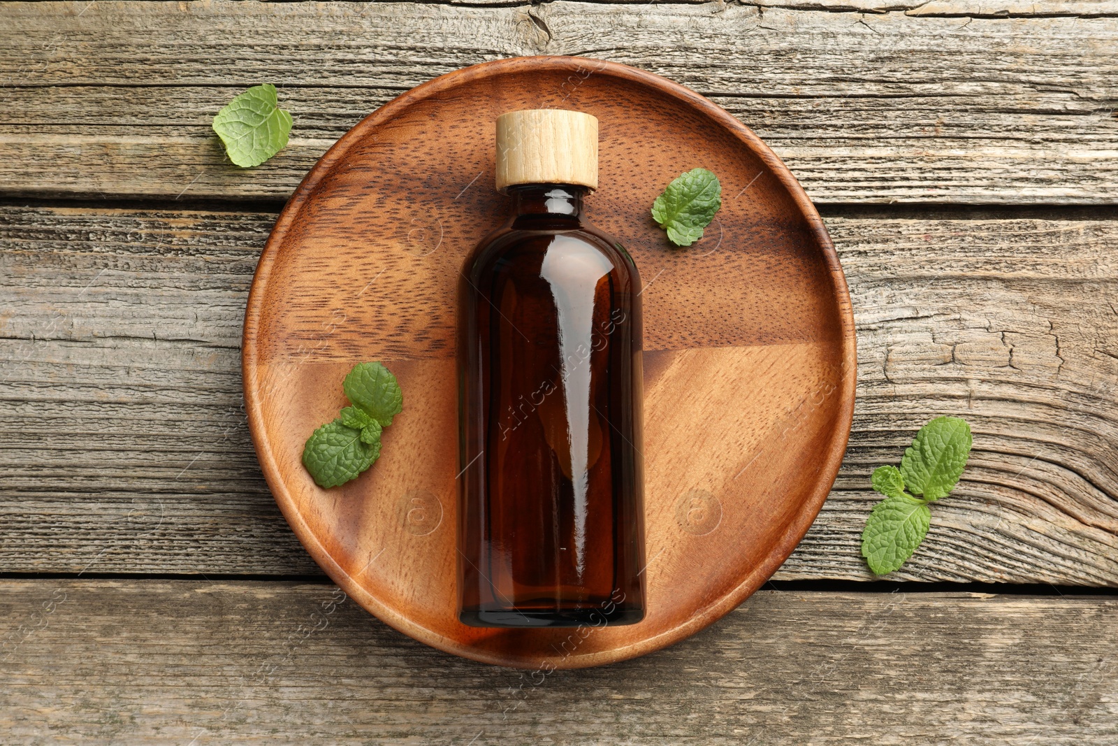 Photo of Bottle of mint essential oil and fresh leaves on wooden table, top view