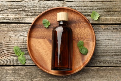 Photo of Bottle of mint essential oil and fresh leaves on wooden table, top view