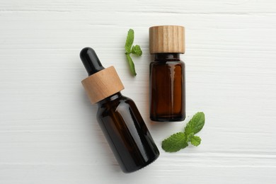 Photo of Bottles of mint essential oil and fresh leaves on white wooden table, top view