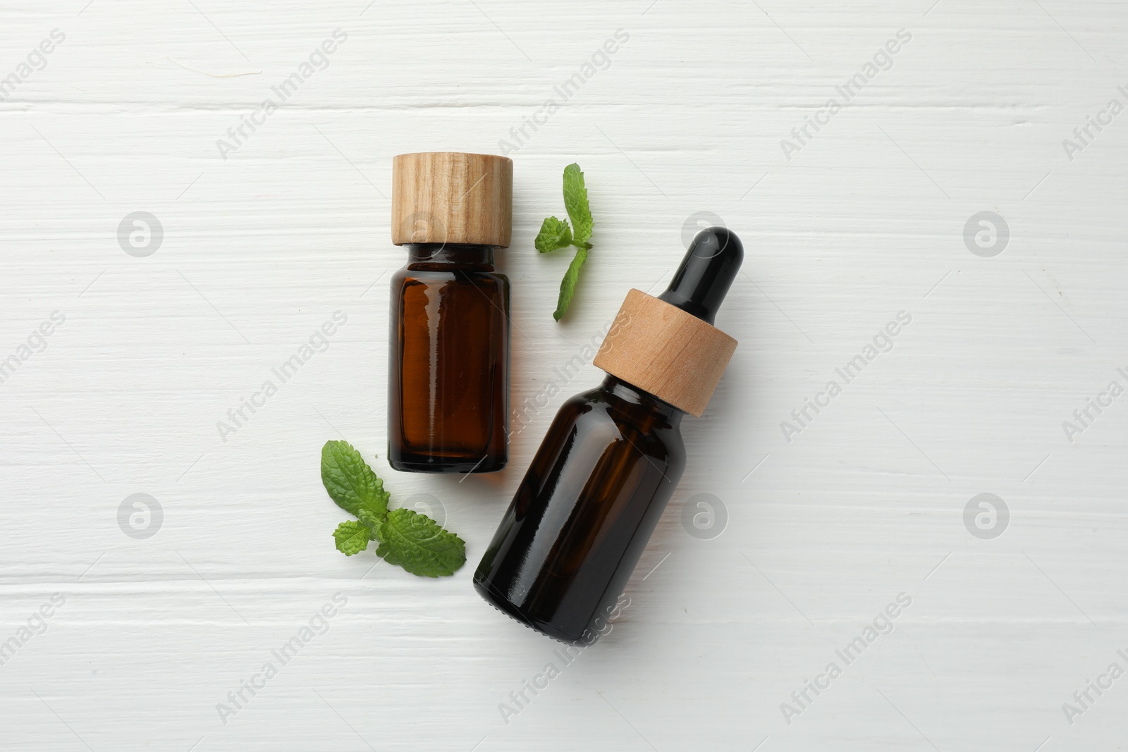 Photo of Bottles of mint essential oil and fresh leaves on white wooden table, top view