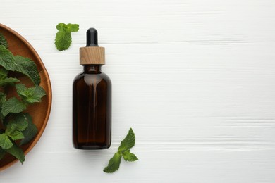 Photo of Bottle of mint essential oil and fresh leaves on white wooden table, top view. Space for text