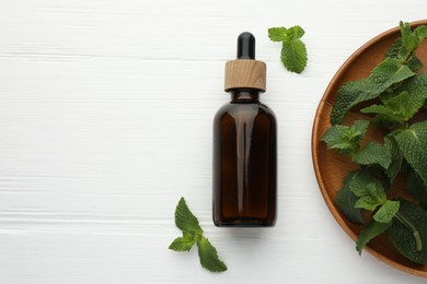 Photo of Bottle of mint essential oil and fresh leaves on white wooden table, top view. Space for text