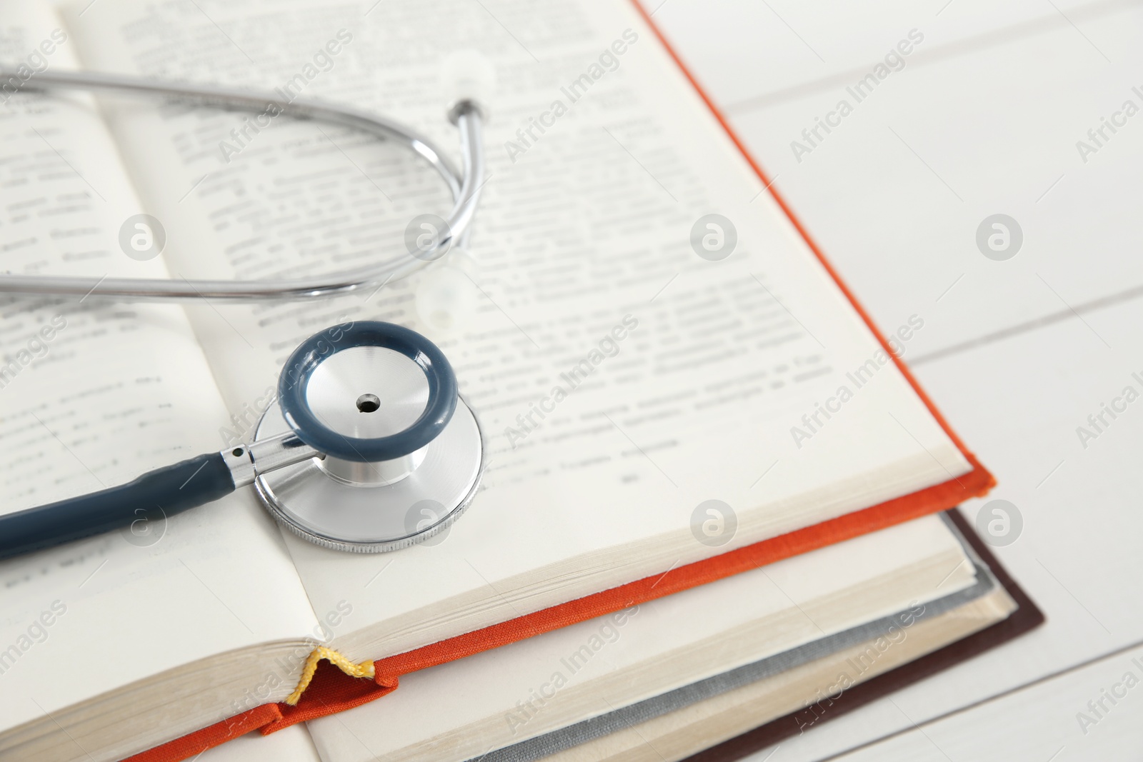 Photo of One new medical stethoscope and books on white wooden table, closeup