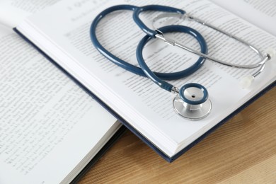 Photo of One new medical stethoscope and books on wooden table, closeup