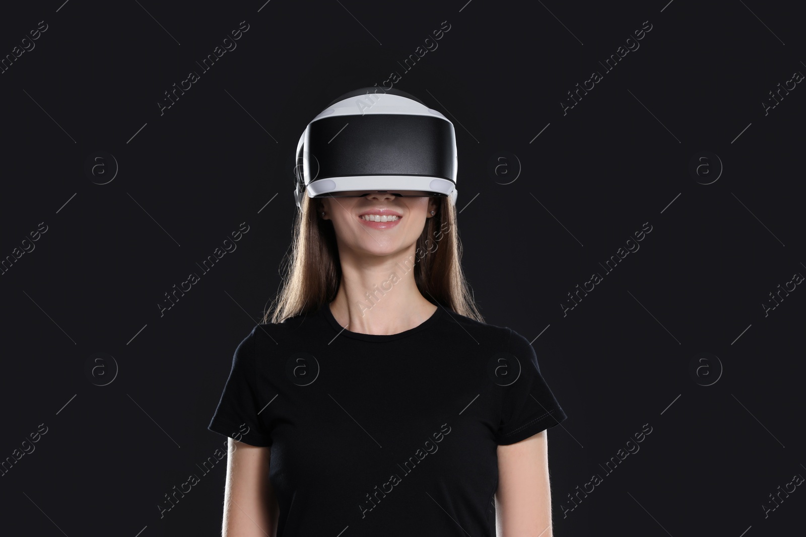 Photo of Smiling woman using virtual reality headset on black background