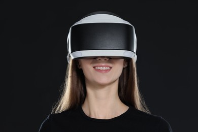 Smiling woman using virtual reality headset on black background