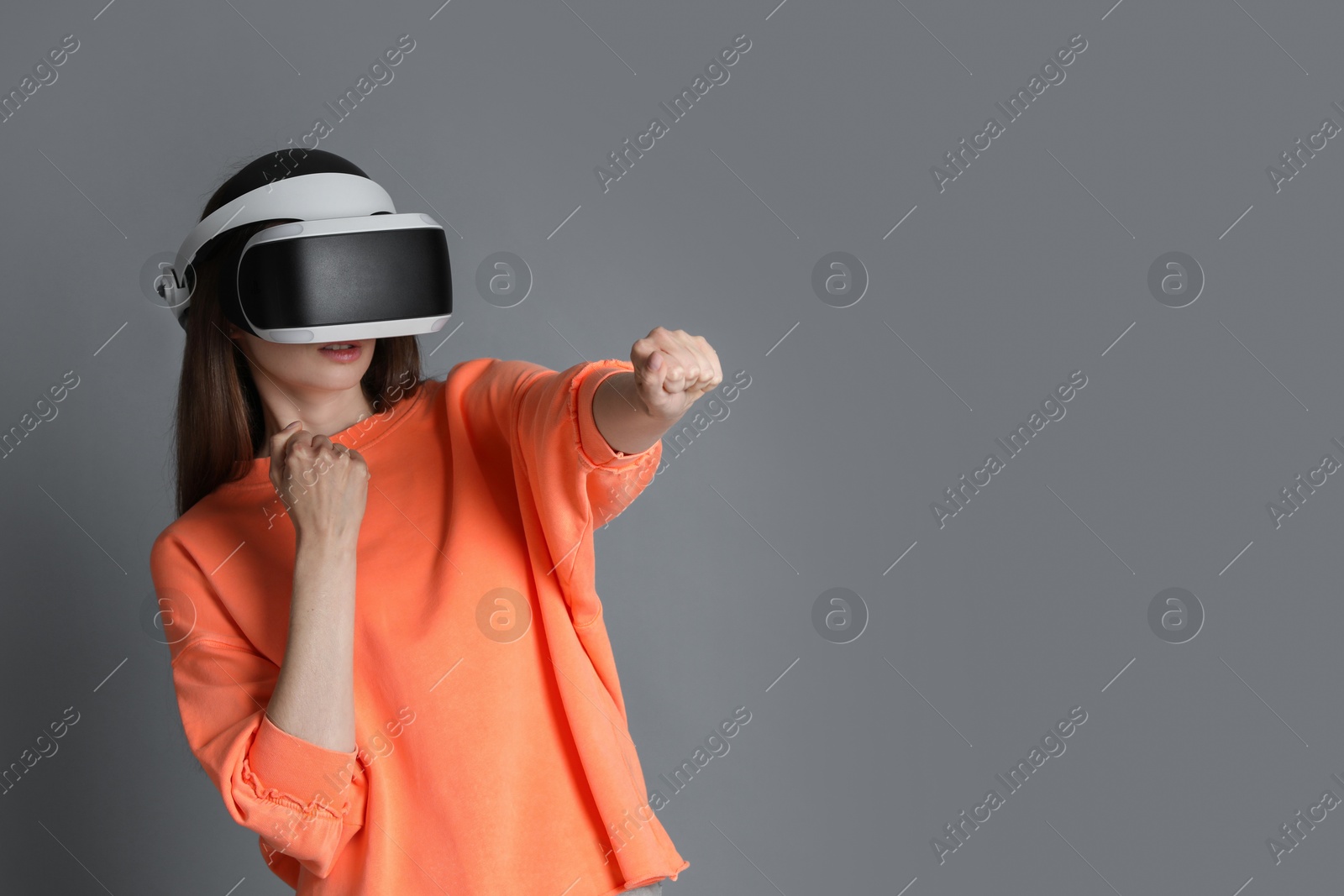 Photo of Woman using virtual reality headset on gray background, space for text