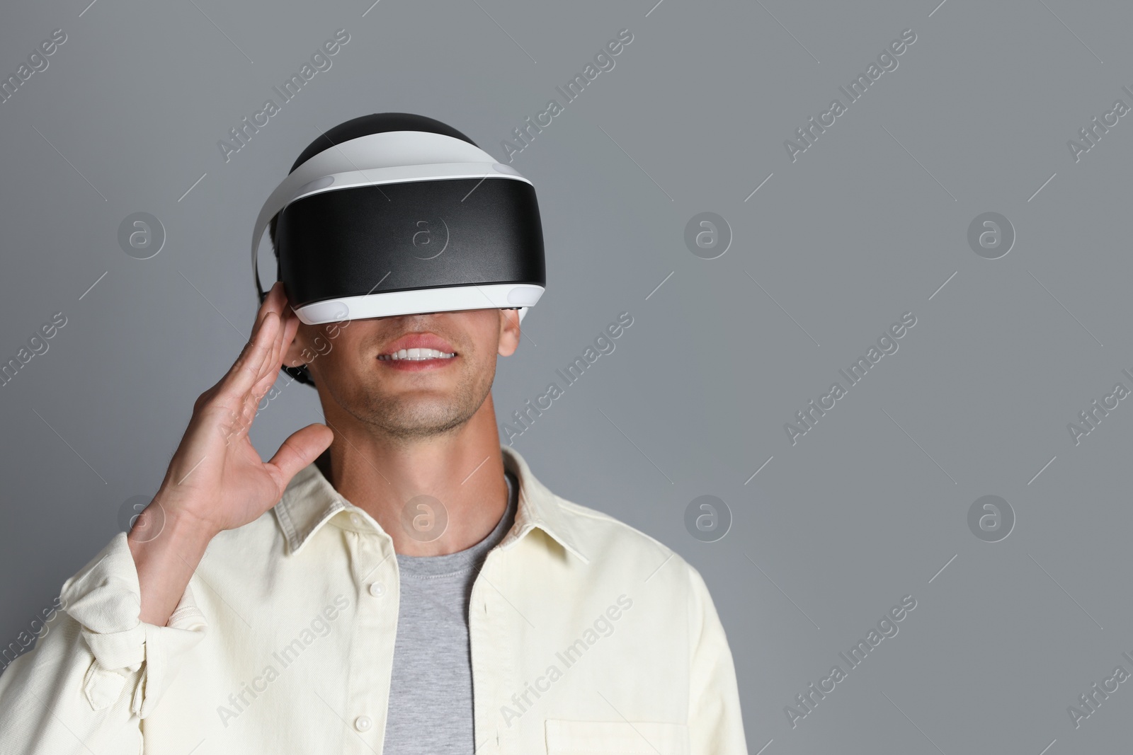 Photo of Smiling man using virtual reality headset on gray background, space for text