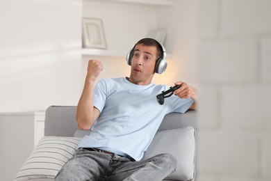 Happy man in headphones playing video games with joystick at home