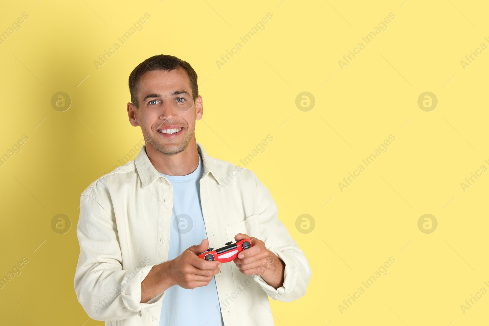 Photo of Happy man playing video games with controller on yellow background, space for text