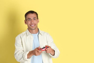 Photo of Happy man playing video games with controller on yellow background, space for text