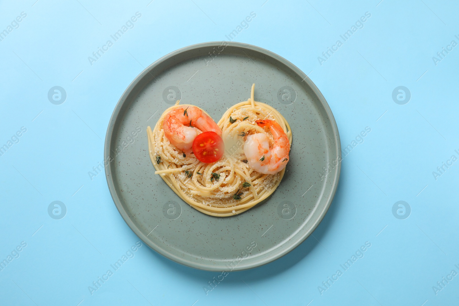 Photo of Heart made of tasty spaghetti, tomato, shrimps and cheese on light blue background, top view