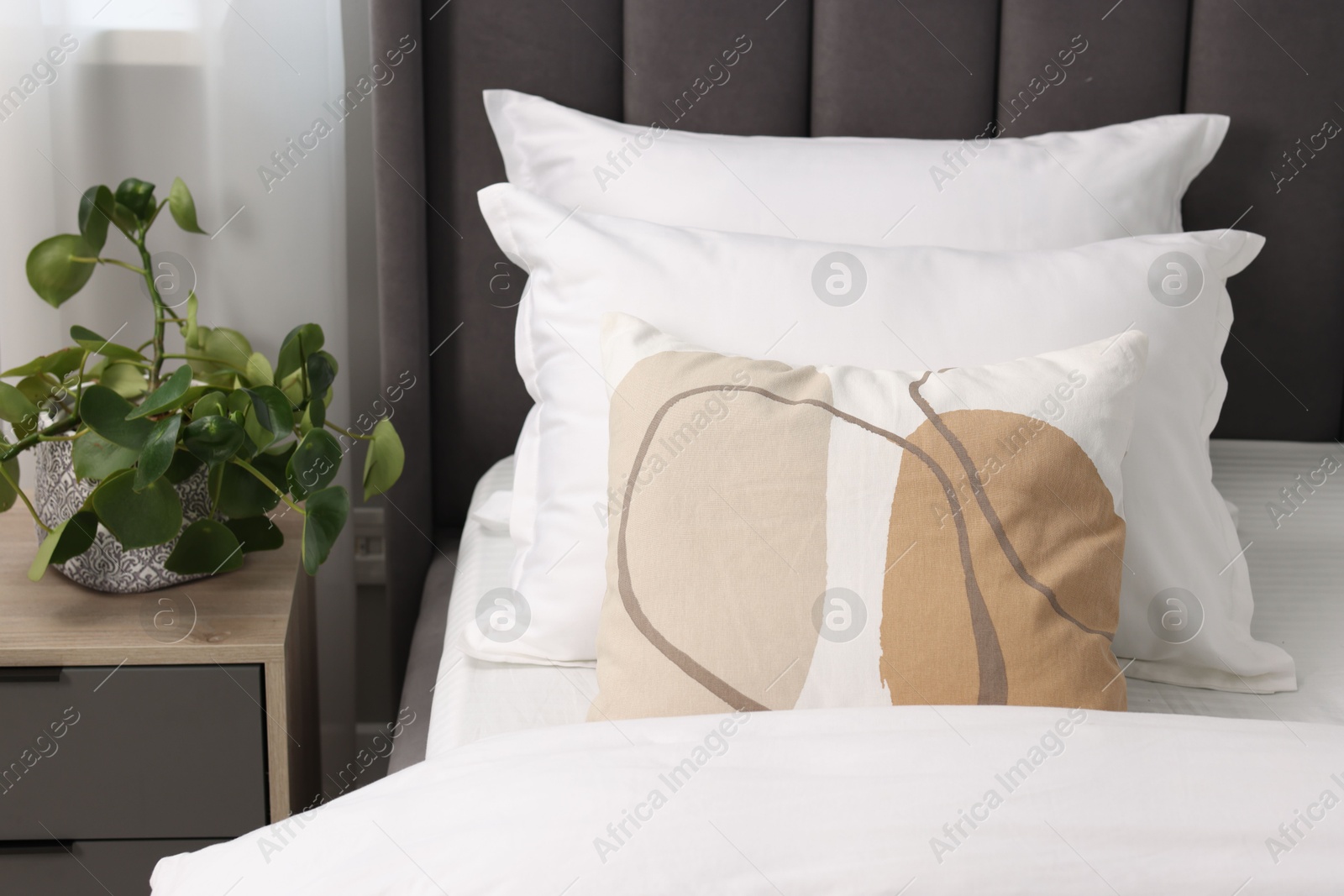 Photo of Many soft pillows on bed and bedside table with houseplant at home, closeup