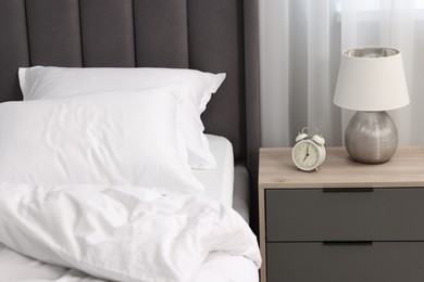 Many soft pillows on bed and bedside table with lamp at home, closeup