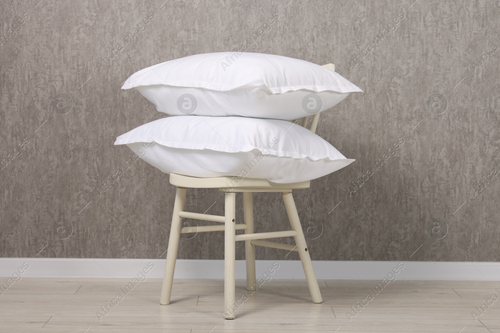 Photo of Many soft pillows on chair near grey wall