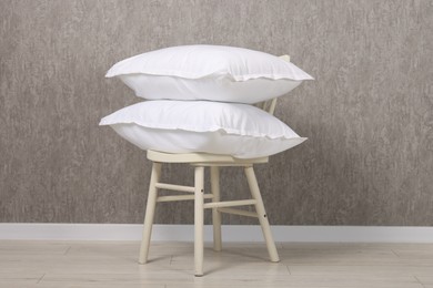 Many soft pillows on chair near grey wall