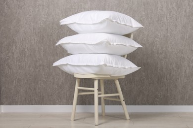 Many soft pillows on chair near grey wall