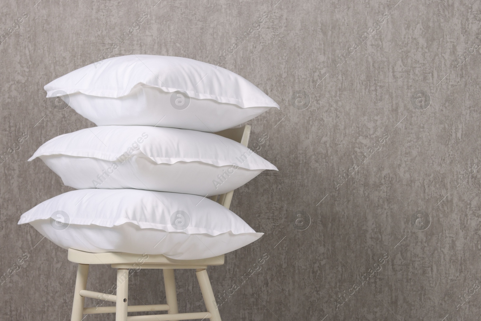 Photo of Many soft pillows on chair near grey wall. Space for text