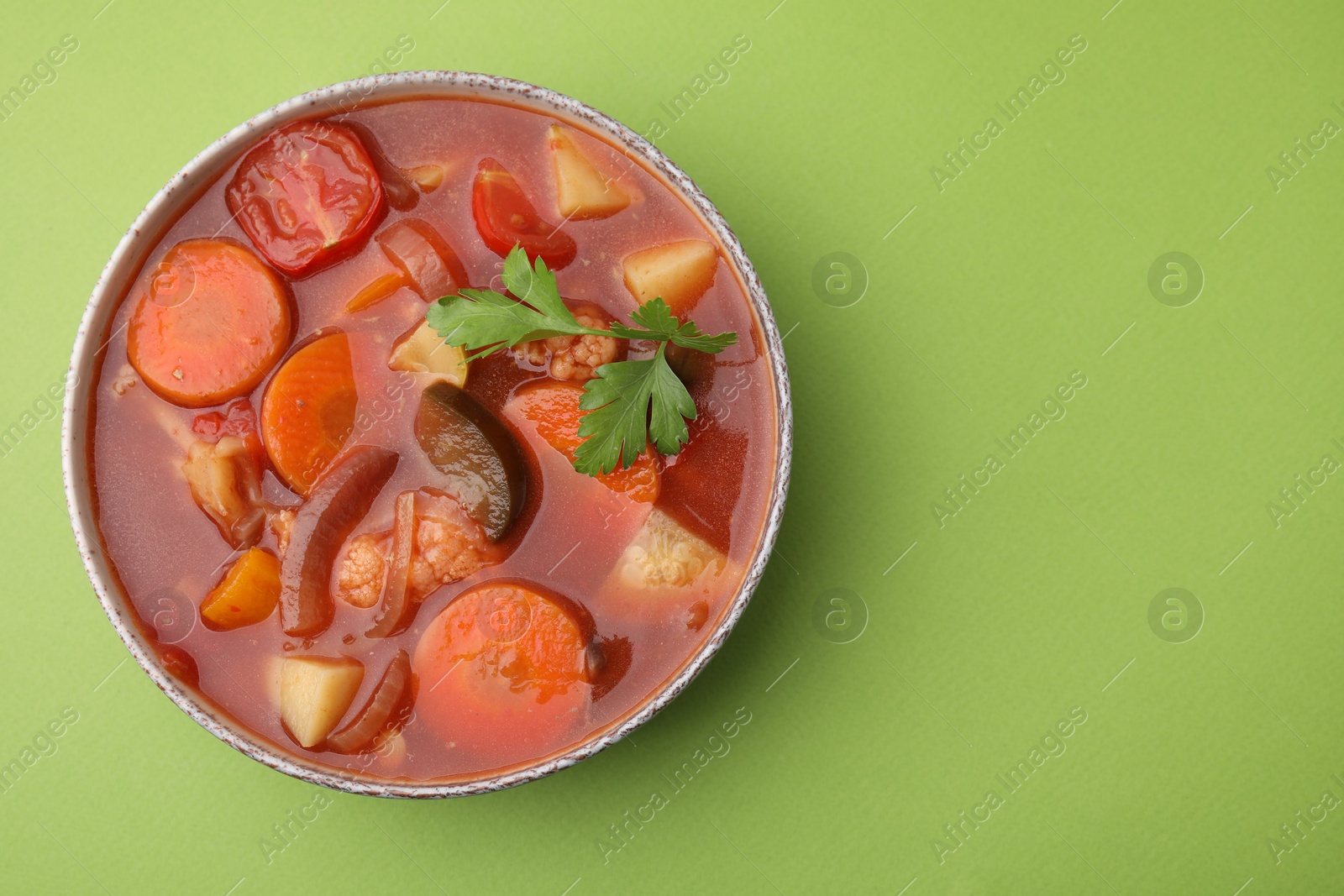 Photo of Delicious homemade stew in bowl on green background, top view. Space for text