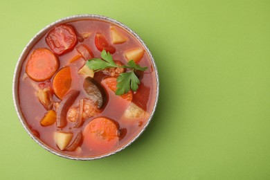 Delicious homemade stew in bowl on green background, top view. Space for text