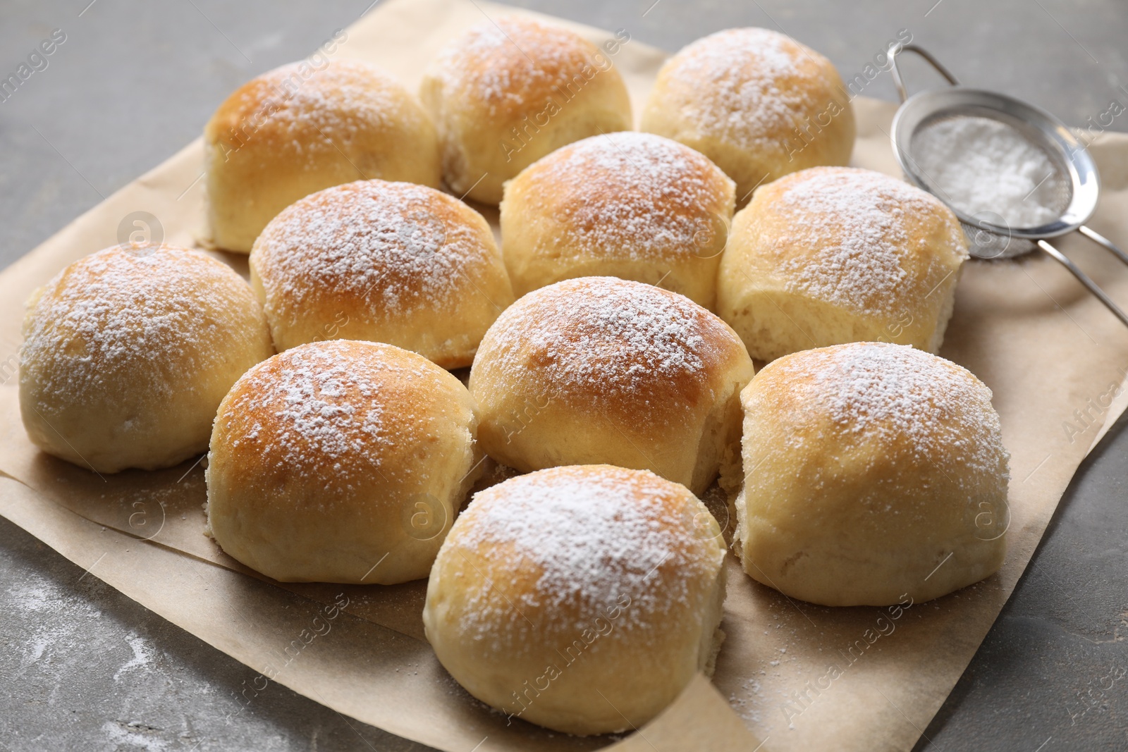 Photo of Delicious dough balls with powdered sugar and sieve on grey table