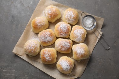 Delicious dough balls with powdered sugar and sieve on grey table, top view