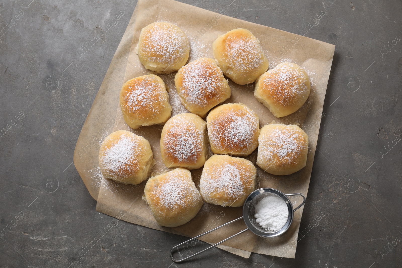 Photo of Delicious dough balls with powdered sugar and sieve on grey table, top view