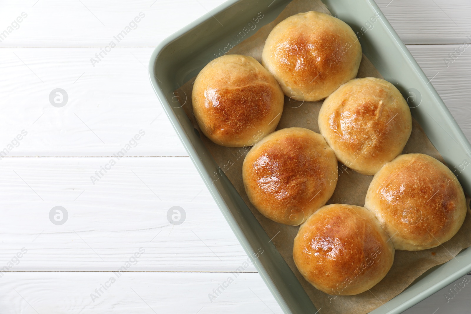 Photo of Delicious dough balls in baking dish on white wooden table, top view. Space for text