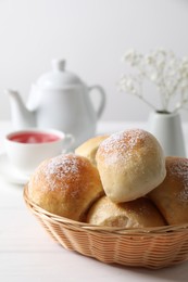 Delicious dough balls with powdered sugar in basket, tea, teapot and gypsophila flowers on white wooden table