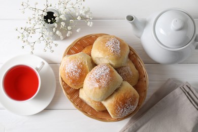 Photo of Delicious dough balls with powdered sugar in basket, tea, teapot and gypsophila flowers on white wooden table, top view