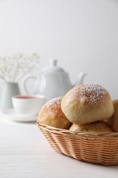 Delicious dough balls with powdered sugar in basket, tea, teapot and gypsophila flowers on white wooden table