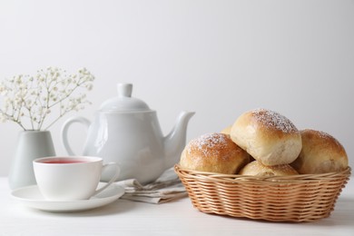 Delicious dough balls with powdered sugar in basket, tea, teapot and gypsophila flowers on white wooden table