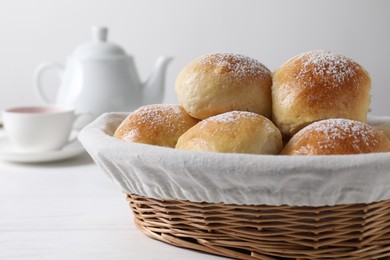 Delicious dough balls with powdered sugar in basket, tea and teapot on white wooden table, closeup