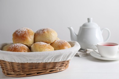 Delicious dough balls with powdered sugar in basket, tea and teapot on white wooden table