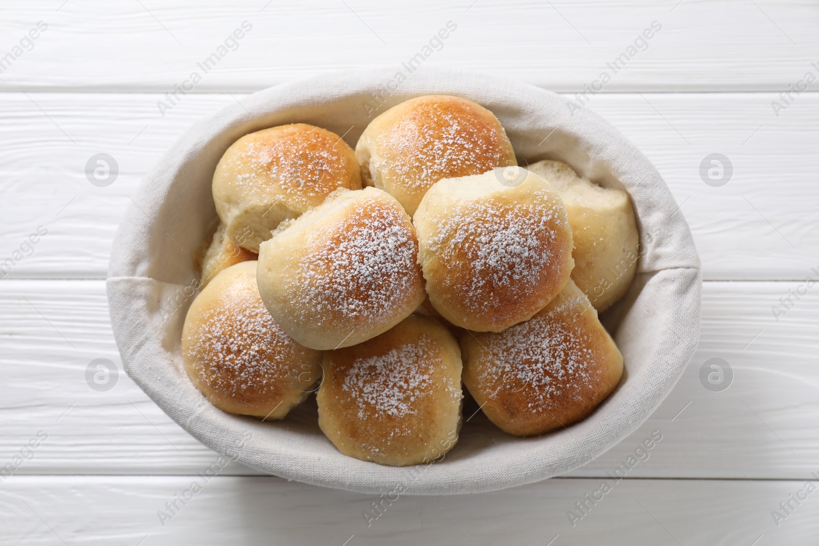 Photo of Delicious dough balls in basket on white wooden table, top view