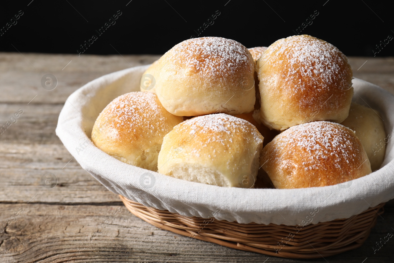 Photo of Delicious dough balls in basket on wooden table, closeup