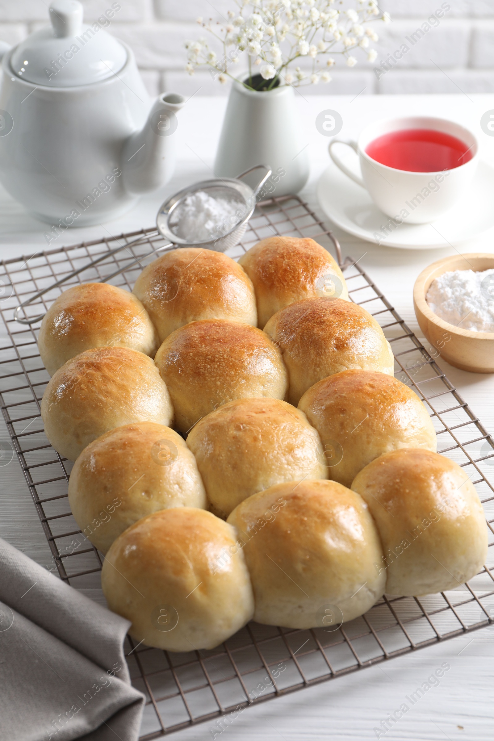 Photo of Delicious dough balls, powdered sugar, tea, teapot and gypsophila flowers on white wooden table