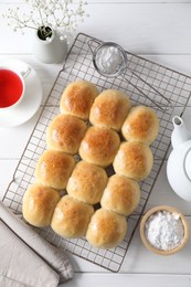 Photo of Delicious dough balls, powdered sugar, tea and gypsophila flowers on white wooden table, top view