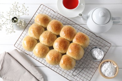 Photo of Delicious dough balls, powdered sugar, tea, teapot and gypsophila flowers on white wooden table, top view