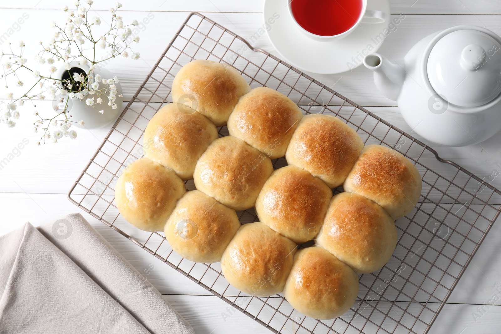 Photo of Delicious dough balls, tea, teapot and gypsophila flowers on white wooden table, top view