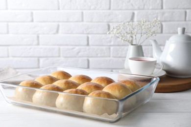 Delicious dough balls in baking dish, tea, teapot and gypsophila flowers on white wooden table