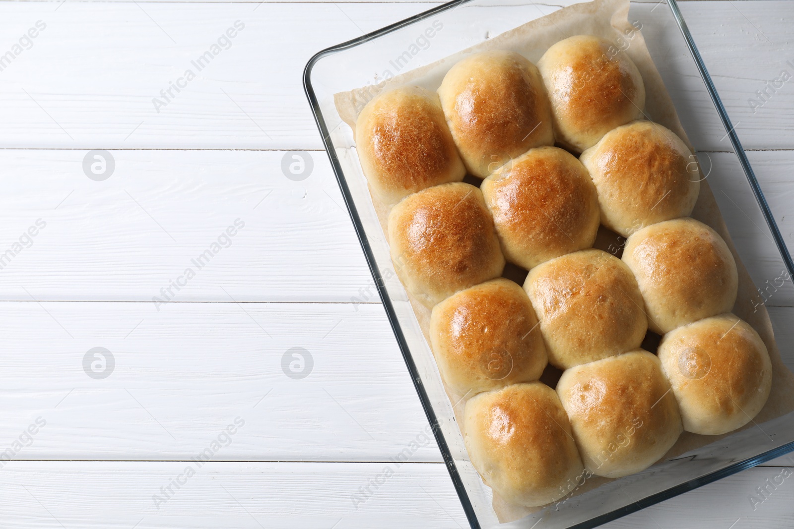 Photo of Delicious dough balls in baking dish on white wooden table, top view. Space for text