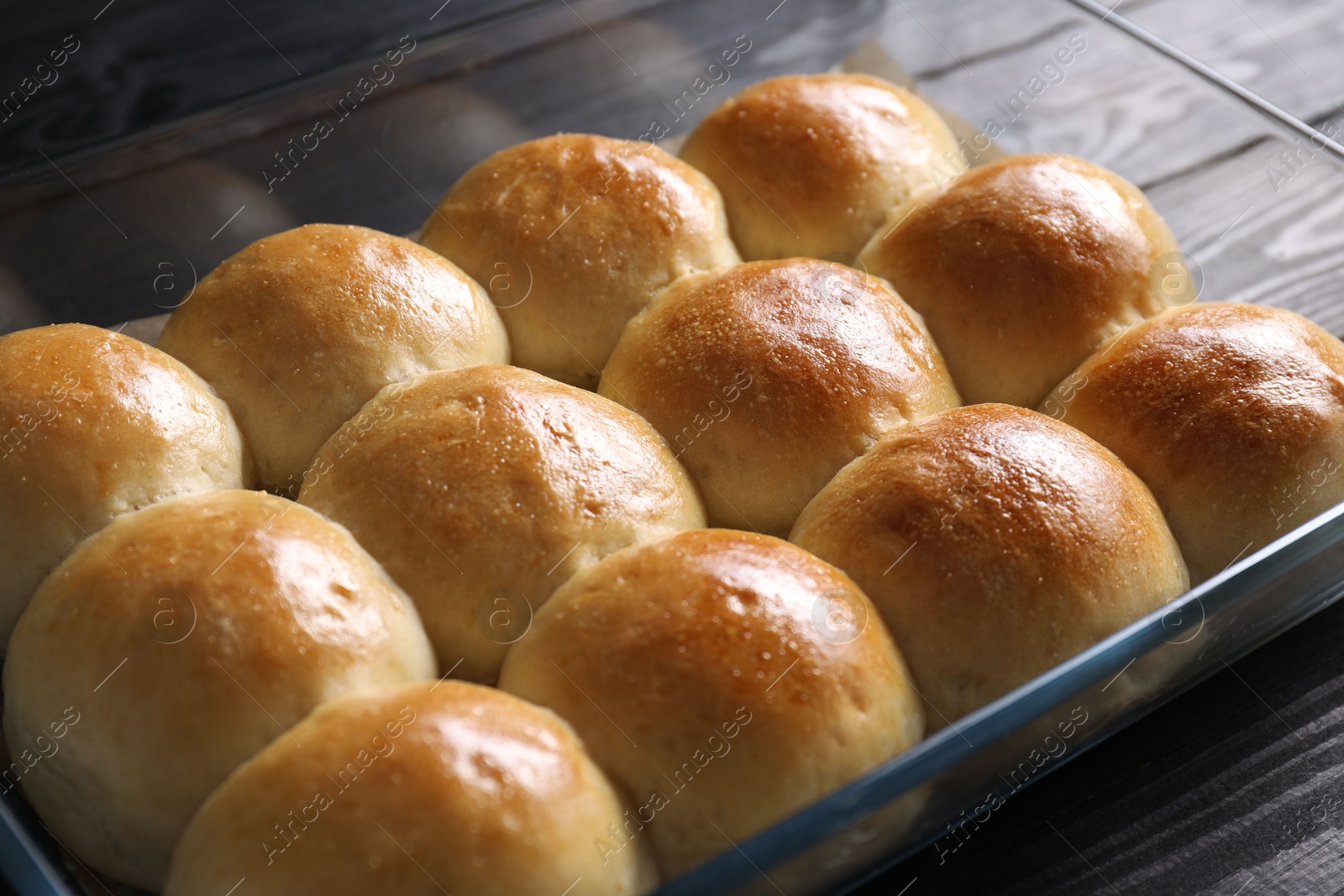 Photo of Delicious dough balls in baking dish on black wooden table, closeup