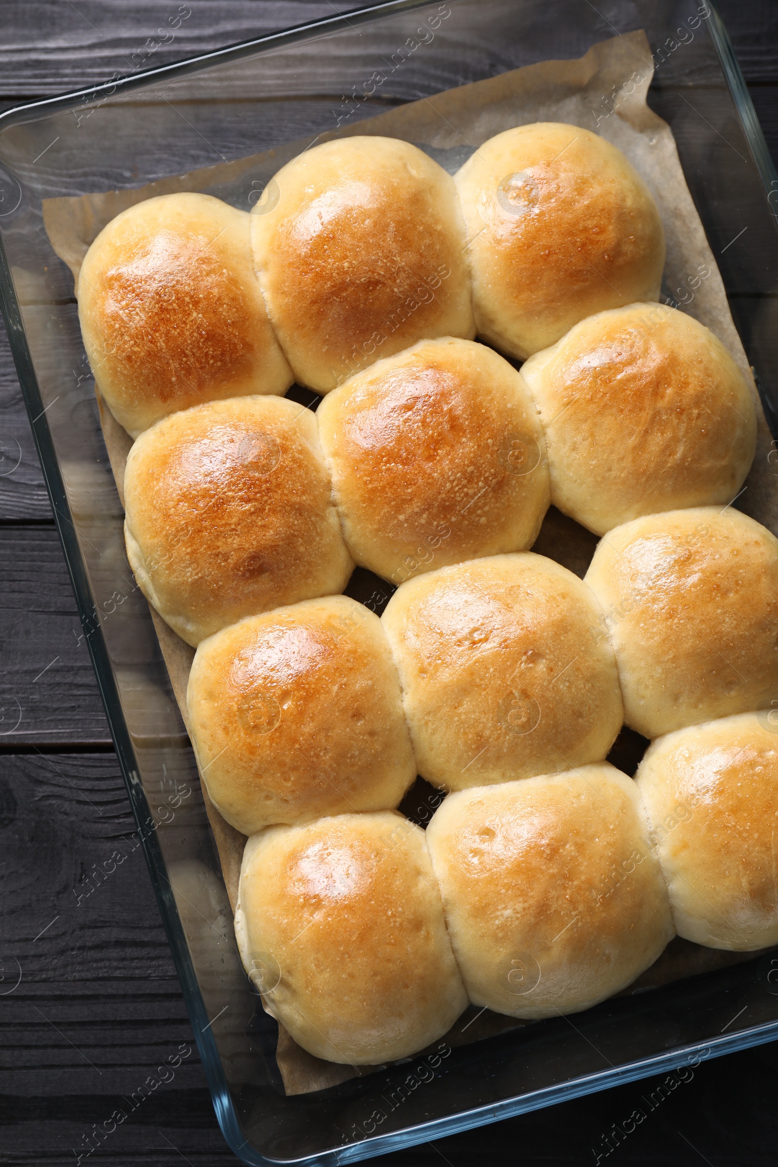 Photo of Delicious dough balls in baking dish on black wooden table, top view