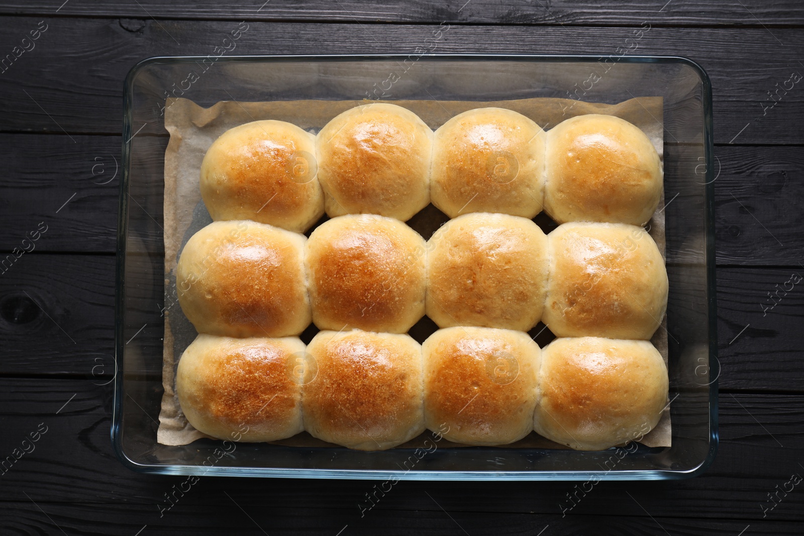 Photo of Delicious dough balls in baking dish on black wooden table, top view