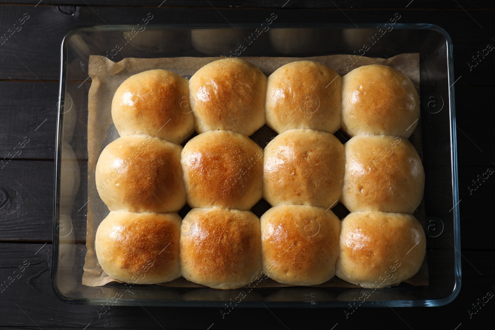 Photo of Delicious dough balls in baking dish on black wooden table, top view